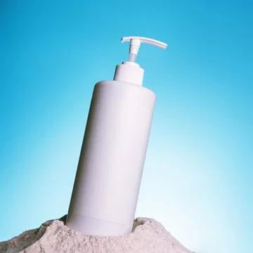 White big plastic pump bottle on light blue wall background and sand. Paste.. Stock Photos