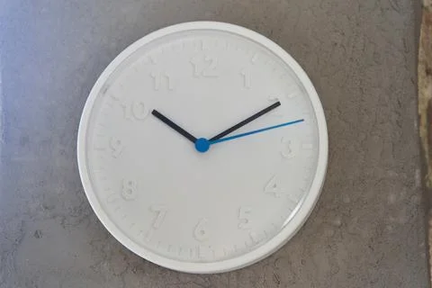 White big wall clock with blue second hand on rough cement wall Stock Photos