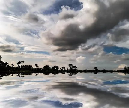 White black clouds in the blue sky and shadows of clouds in the water. Stock Photos