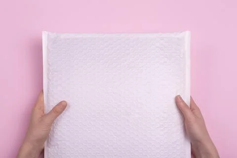 White blank envelope with postal parcel in hands on a pink background. Postal Stock Photos