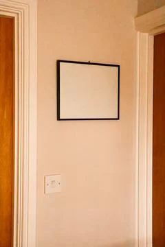 White blank frame hanging on a light colored wall inside an empty modern ho.. Stock Photos