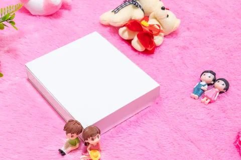 White blank rectangle box above a fluffy pink carpet surrounded by dolls Stock Photos