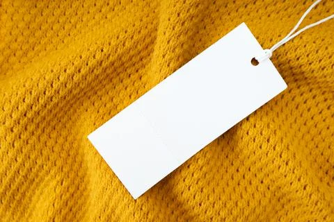 White blank rectangular clothing tag on yellow knitted fabric background Stock Photos