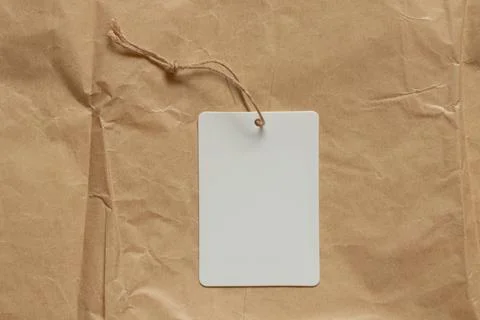 White blank tag on string lies on brown crumpled paper as mockup for design Stock Photos