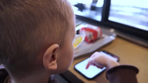 White blond boy 4-5 years old with a mobile phone in a fast food restaurant Stock Footage 306616377