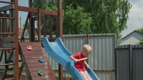 White Blond Boy Sliding Down Slide Wooden Playset Backyard, Blue Slide, Climbing Vídeo Stock 324527680
