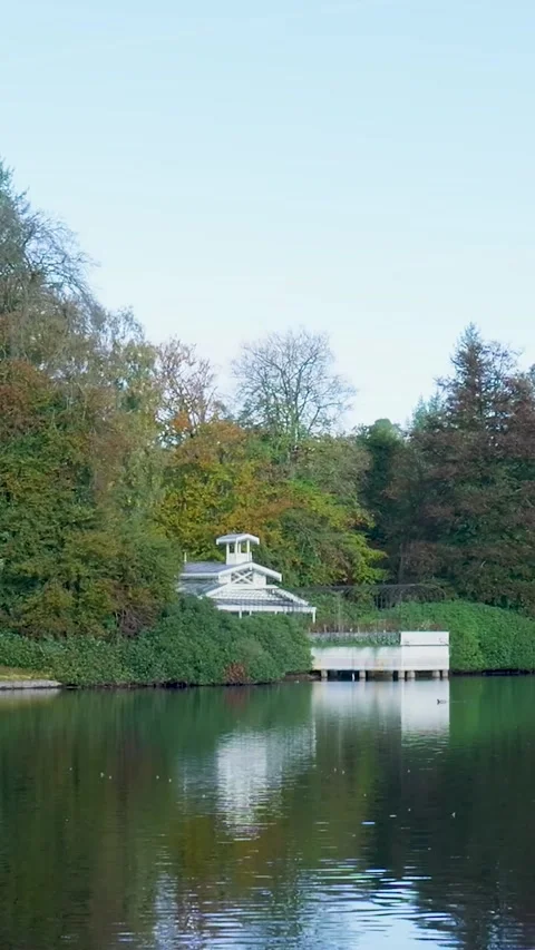 White boathouse reflection on a calm lake surrounded by autumn forest Stock Footage 327109014
