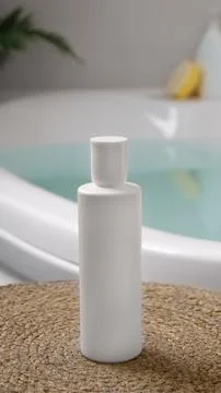 White bottle of bubble bath on wicker mat near tub indoors Stock Photos