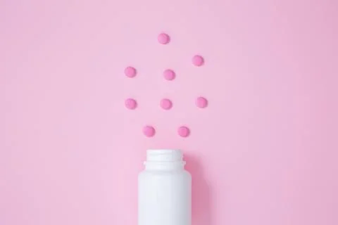 White bottle container with medication tablets on pink background. Concept of Stock Photos