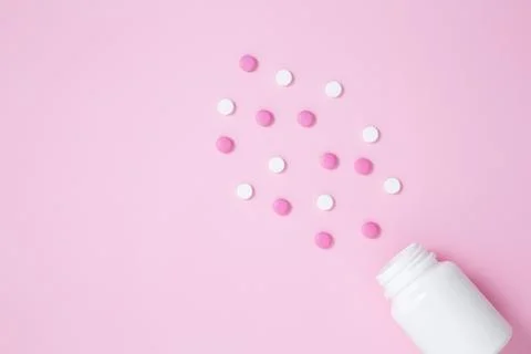 White bottle container with medication tablets on pink background. Concept of Stock Photos