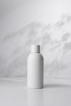 White bottle on a light background with shadows of plant leaves, representing Foto stock