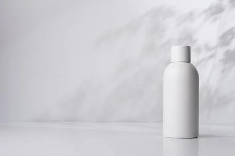 White bottle on a light background with shadows of plant leaves, representing Stock Photos