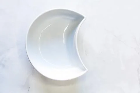 White bowl in the shape of a half-moon. Top view, space for text. Stock Photos