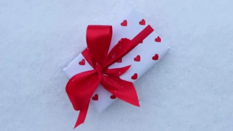 A white box in hearts with a red bow lies on the snow. The concept of Stock Footage 167492831