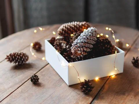 White box with pine cones and light bulbs on wooden table. Scandy style. Prep Stock Photos