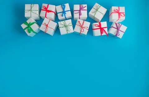 White boxes with colored ribbons lie on a blue background. Top view. Space fo Stock Photos