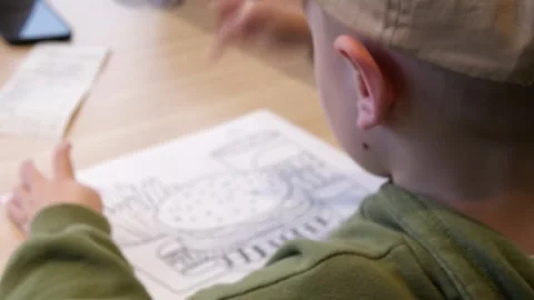 A white boy of 4-5 years old at a table with a coloring picture, points at it. Vídeo Stock 311588295