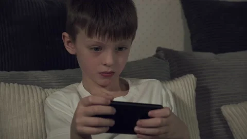 White boy 7-9 years old enthusiastically playing a game on a smartphone, sitting Stock Footage 146316705