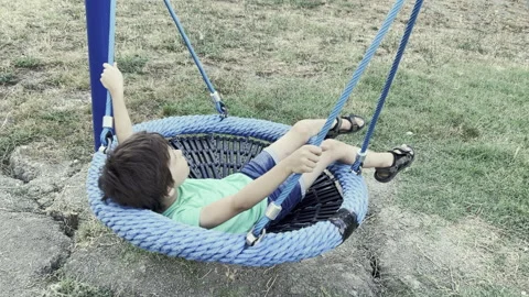 White boy swinging in a web swing in the playground in the park Stock Footage 217700124