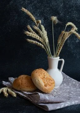 White bread rolls decorated with wheat ears in white vase on dark background Stock Photos