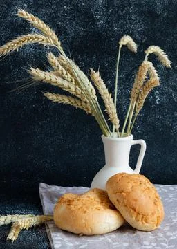White bread rolls decorated with wheat ears in white vase on dark background Stock Photos
