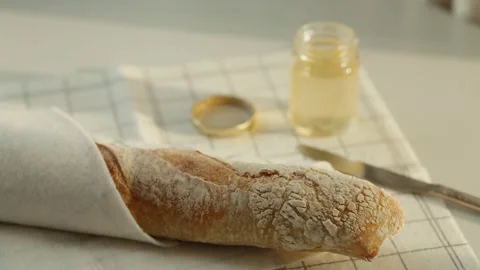White bread wrapped in a towel and a jar of acacia honey with kitchen utensils. Stock Footage 344834008