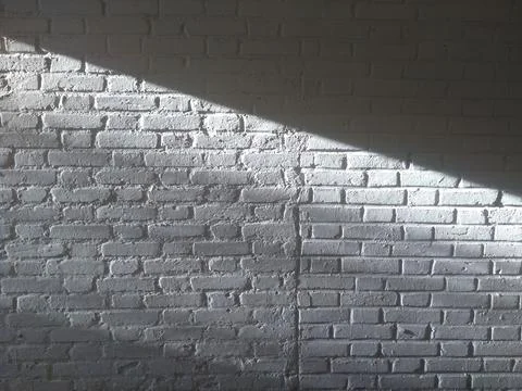 White brick wall, with diagonal ray of sunlight forming contrast of light and Stock Photos