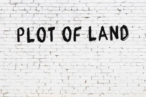  White brick wall with inscription plot of land handwritten with black paint Foto stock