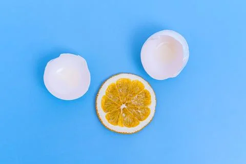 White broken eggshells and a dry round orange like a yolk on a blue backgro.. Foto stock
