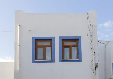 A white building with blue window frames against a blue sky in the Greek style Stock Photos