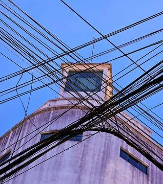 A white building with a tangle of electrical wires in front of it. Stock Photos
