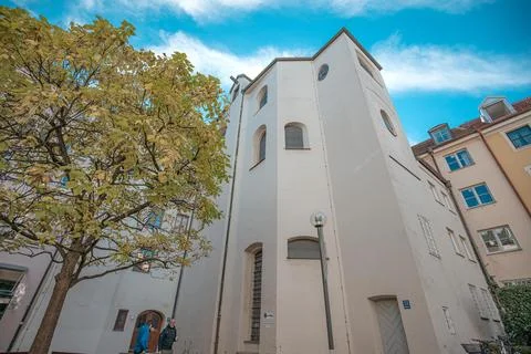 A white building with a tree in front and blue sky above. The building is tall Stock Photos