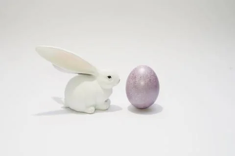A white bunny rabbit looking at easter purple egg. Stock Photos