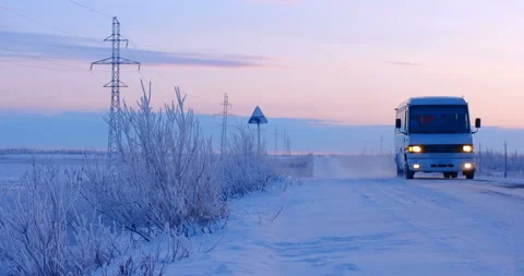A white bus with headlights on is moving along a snowy country road, turning on  Stock Footage 105988143