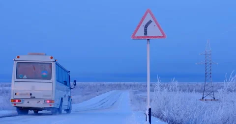 The white bus is moving along a snowy country road that goes to the right Stock Footage 105988025