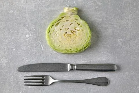 White cabbage in cross section and fork and knife on a gray concrete countertop Stock Photos