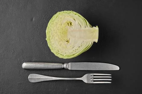 White cabbage in a cut, fork and knife on a black stone tabletop Stock Photos