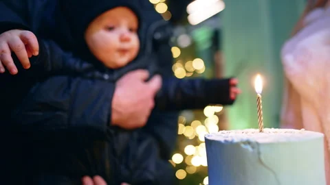 A white cake with burning candle in front of the tiny baby. Stock Footage 257420289