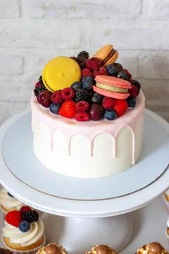 White cake decorated with huge macarons, raspberries, strawberries and blue.. Stock Photos