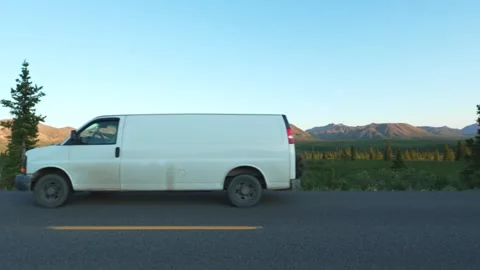 White camper van driving road past mountains and wilderness during an Alaska Stock Footage 342131475