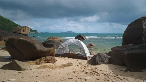 White camping tent nestled between large rocks on sandy beach, offering stunning Stock Footage 312748352