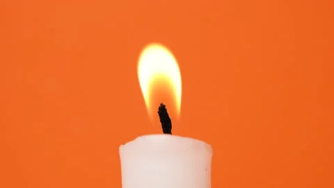 A white candle burning on a bright orange background. A candle is blown out Stock Footage 211185482