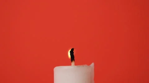 A white candle burning on a bright red background. A candle is blown out Stock Footage 223949143