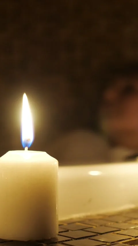 White candle burning in a dark, relaxing bathroom next to a bathtub, creating a Video stock 341678527