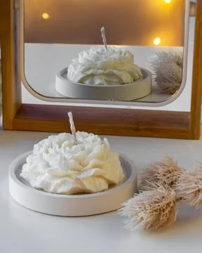 White candle in the shape of a flower on the table near the mirror with ref.. Stock Photos