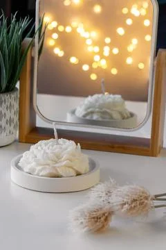 White candle in the shape of a flower on the table near the mirror with refle Stock Photos
