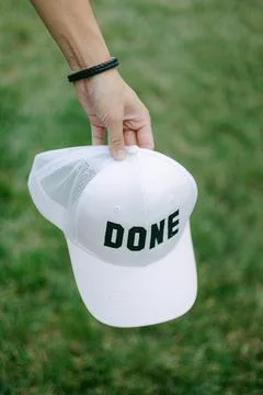White cap with bold word done held in a hand against a green grassy background Stock-Fotos