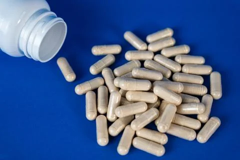 White capsules scattered from an open bottle on a blue background. Medical Stock Photos