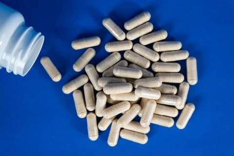 White capsules spilling from plastic bottle on blue background. Concept of Stock Photos