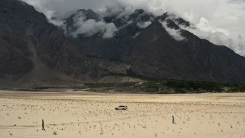 White car driving fast, in a cold desert, with black mountains, Aerial dolly in Stock Footage 131713728